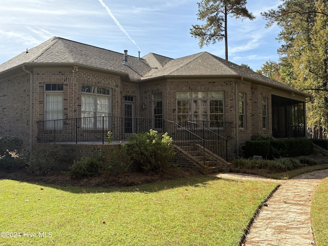 rear view of property with brick siding, a yard, a sunroom, and a shingled roof