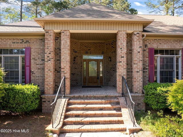 entrance to property featuring a shingled roof, brick siding, and covered porch