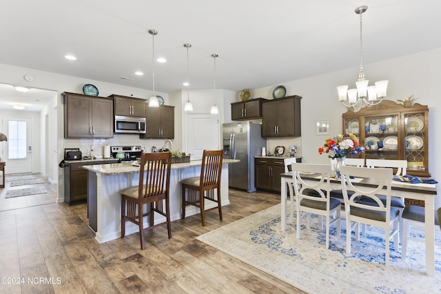 kitchen with wood finished floors, an inviting chandelier, stainless steel appliances, dark brown cabinets, and tasteful backsplash