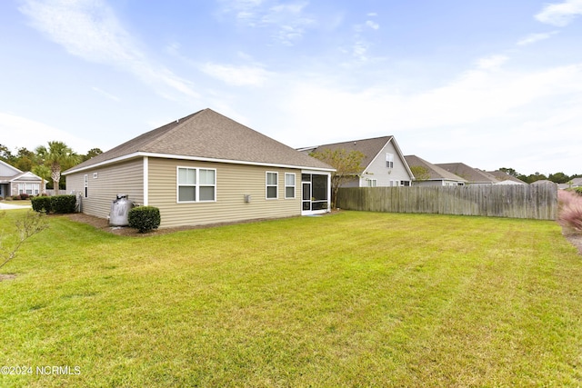 back of house featuring a sunroom, a yard, fence, and roof with shingles