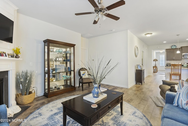 living room featuring a fireplace, baseboards, light wood finished floors, and ceiling fan