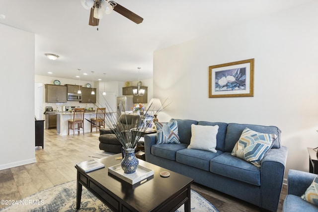 living room with recessed lighting, ceiling fan with notable chandelier, baseboards, and light wood finished floors