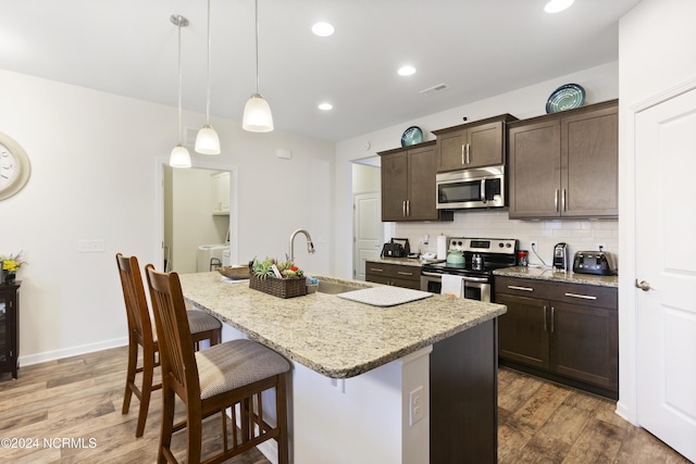 kitchen with visible vents, a sink, appliances with stainless steel finishes, a kitchen breakfast bar, and backsplash