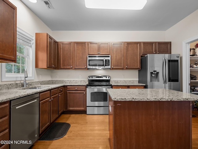 kitchen with light stone counters, stainless steel appliances, sink, light hardwood / wood-style flooring, and a center island