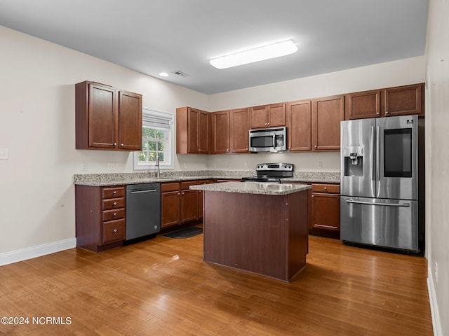 kitchen with appliances with stainless steel finishes, a center island, light stone counters, and dark wood-type flooring