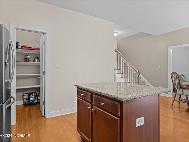 kitchen with stainless steel fridge, a kitchen island, light stone counters, and light wood-type flooring