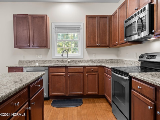 kitchen with stainless steel appliances, light stone counters, light hardwood / wood-style floors, and sink