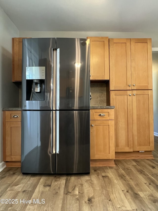 kitchen featuring dark stone countertops, stainless steel fridge with ice dispenser, backsplash, and light hardwood / wood-style flooring