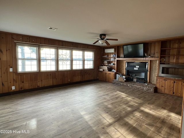 unfurnished living room featuring hardwood / wood-style flooring, built in features, ceiling fan, and wood walls