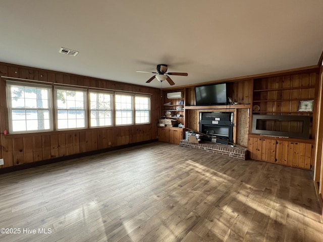 unfurnished living room with built in shelves, hardwood / wood-style flooring, ceiling fan, and wood walls