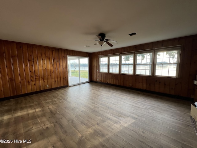 empty room featuring hardwood / wood-style flooring, ceiling fan, and wood walls