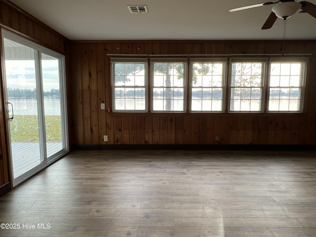 empty room with ceiling fan, plenty of natural light, light wood-type flooring, and wooden walls