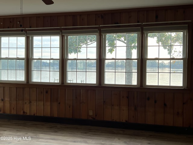 doorway with ceiling fan, hardwood / wood-style floors, a water view, and wood walls