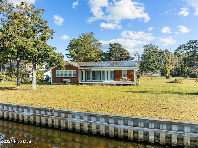 rear view of house featuring a lawn, a water view, and solar panels