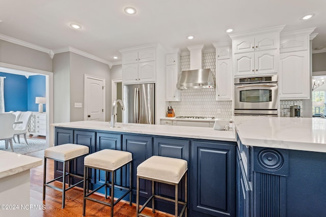 kitchen featuring wall chimney range hood, crown molding, appliances with stainless steel finishes, white cabinetry, and tasteful backsplash