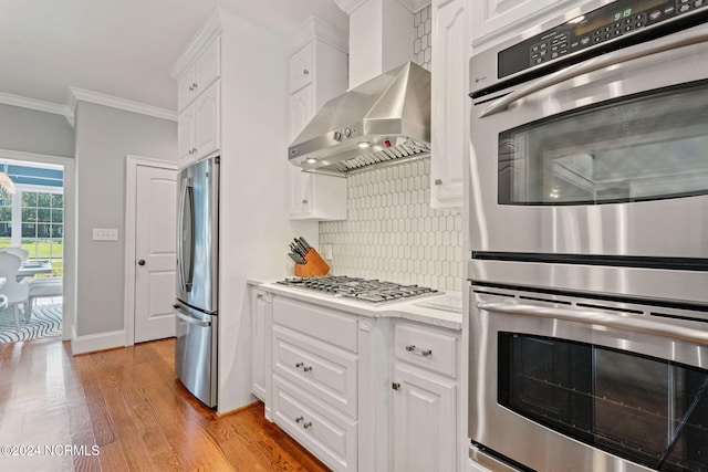 kitchen featuring appliances with stainless steel finishes, tasteful backsplash, ornamental molding, white cabinets, and wall chimney exhaust hood