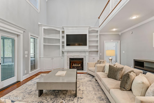 living room with a premium fireplace, ornamental molding, hardwood / wood-style floors, and a towering ceiling