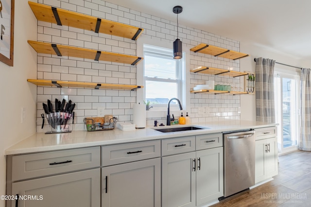 kitchen featuring hardwood / wood-style floors, decorative backsplash, stainless steel dishwasher, pendant lighting, and sink