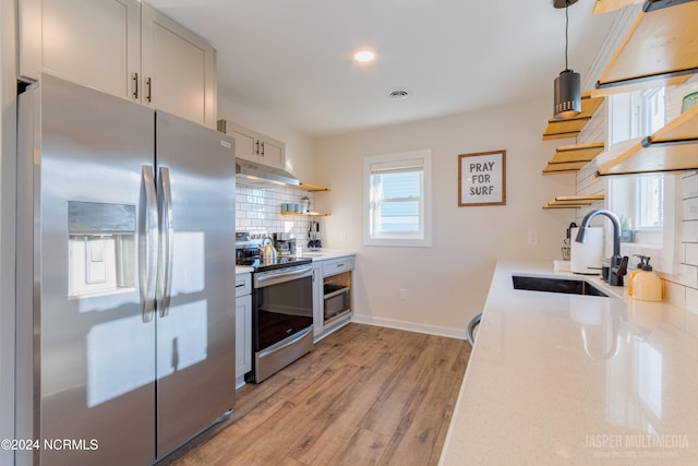 kitchen featuring tasteful backsplash, appliances with stainless steel finishes, light wood-type flooring, pendant lighting, and sink