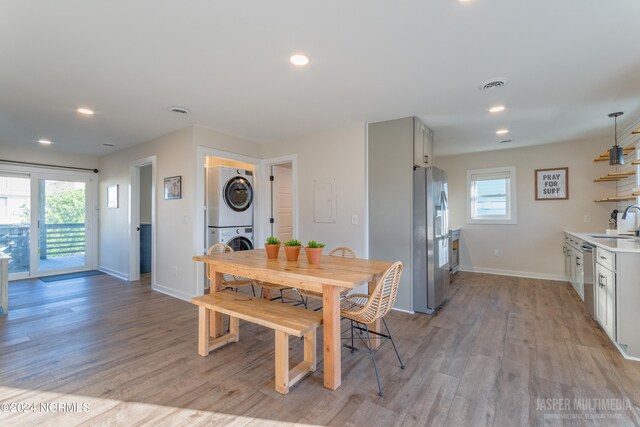 dining area featuring light hardwood / wood-style floors, stacked washer / drying machine, sink, and a wealth of natural light