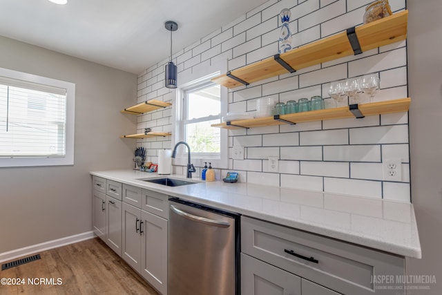 kitchen with tasteful backsplash, hanging light fixtures, light hardwood / wood-style flooring, dishwasher, and sink