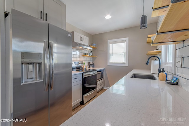 kitchen with sink, white cabinets, pendant lighting, appliances with stainless steel finishes, and light stone counters