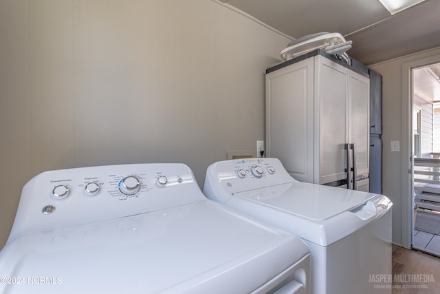 laundry room featuring hardwood / wood-style floors, washing machine and clothes dryer, and cabinets