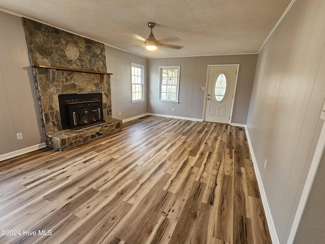 unfurnished living room featuring hardwood / wood-style flooring, ornamental molding, wooden walls, and a textured ceiling