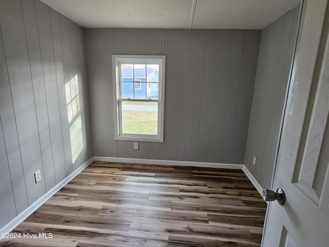 unfurnished room with wooden walls, light hardwood / wood-style floors, and a textured ceiling