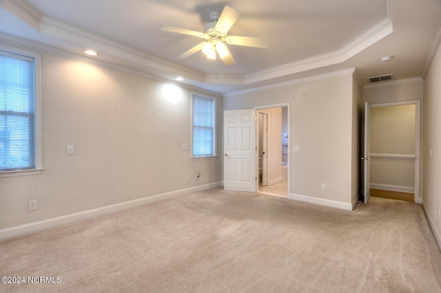 unfurnished bedroom featuring multiple windows, ceiling fan, a tray ceiling, and crown molding