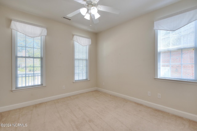 empty room featuring ceiling fan, plenty of natural light, and light colored carpet