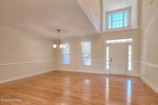 foyer featuring a towering ceiling, an inviting chandelier, ornamental molding, and light wood-type flooring