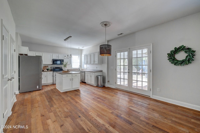 kitchen with a kitchen island, appliances with stainless steel finishes, white cabinetry, light hardwood / wood-style flooring, and decorative light fixtures