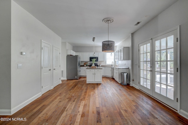 kitchen with white cabinets, appliances with stainless steel finishes, wood-type flooring, pendant lighting, and sink