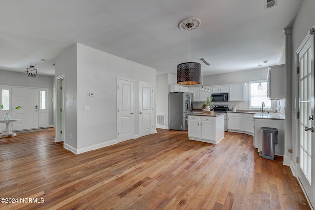 kitchen with a kitchen island, appliances with stainless steel finishes, white cabinetry, light wood-type flooring, and decorative light fixtures