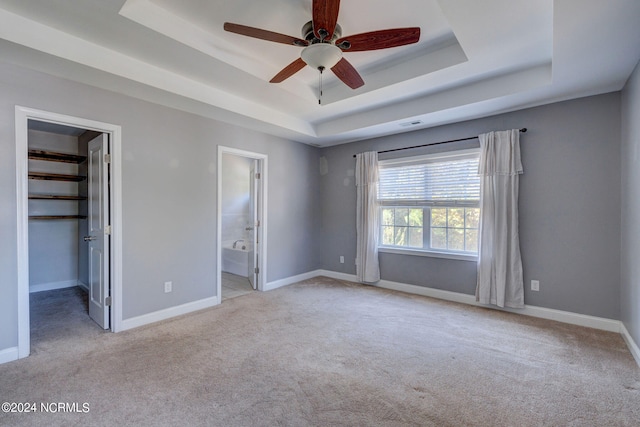 unfurnished bedroom featuring ensuite bathroom, a walk in closet, a tray ceiling, a closet, and ceiling fan