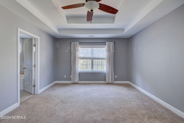 carpeted spare room with a tray ceiling and ceiling fan