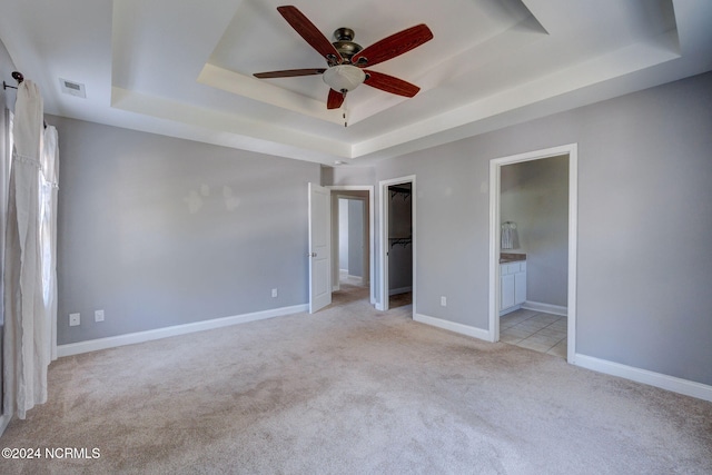 unfurnished bedroom with a walk in closet, ensuite bathroom, ceiling fan, and a raised ceiling