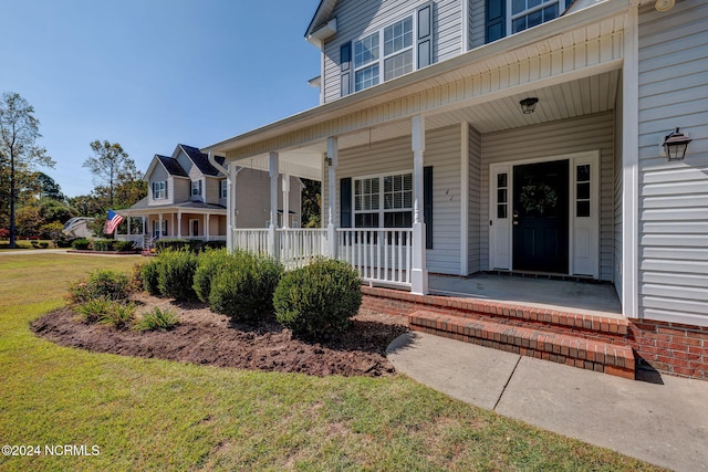 view of exterior entry featuring covered porch and a lawn