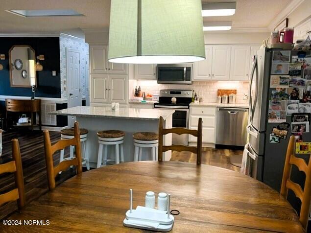 kitchen with backsplash, a breakfast bar area, ornamental molding, white cabinetry, and stainless steel appliances