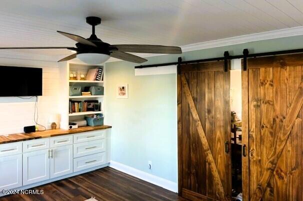 bar featuring dark wood-type flooring, a barn door, wooden counters, white cabinets, and ornamental molding