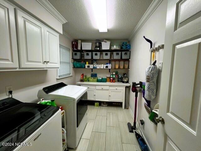 laundry area featuring a textured ceiling, cabinets, independent washer and dryer, and ornamental molding