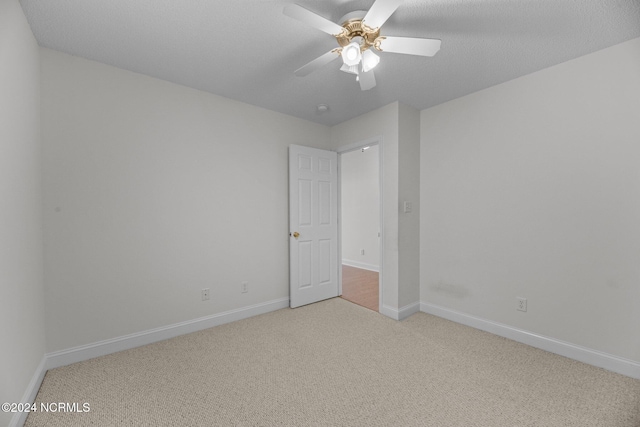 spare room with a textured ceiling, light colored carpet, and ceiling fan