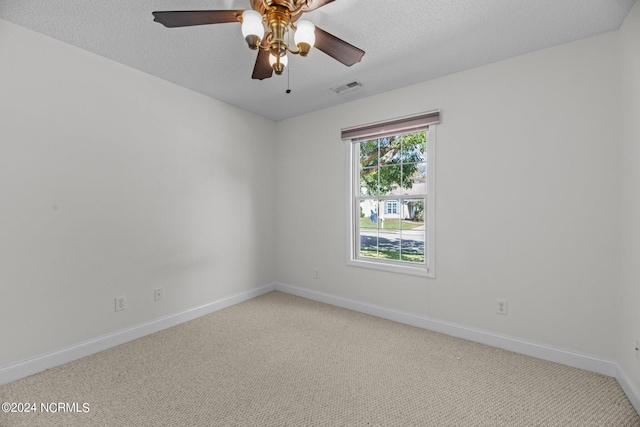 spare room with a textured ceiling, light colored carpet, and ceiling fan