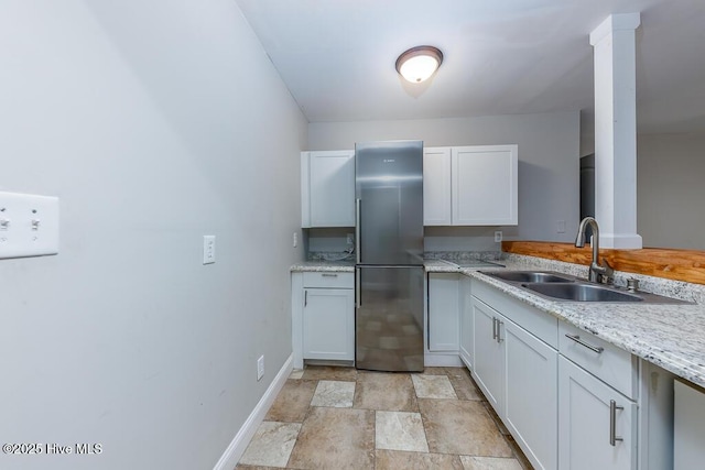 kitchen with light stone countertops, sink, stainless steel fridge, and white cabinets