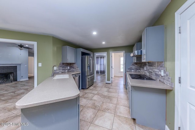 kitchen featuring a brick fireplace, stainless steel appliances, backsplash, and sink