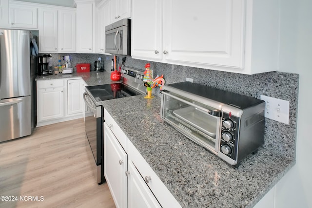 kitchen with appliances with stainless steel finishes, backsplash, white cabinets, and light wood-type flooring