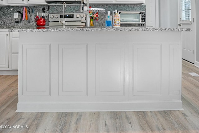 interior space with white cabinetry, electric range, light stone countertops, and light hardwood / wood-style floors