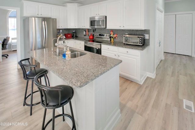 kitchen featuring stainless steel appliances, an island with sink, sink, and white cabinetry