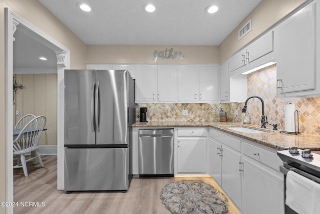 kitchen with decorative backsplash, white cabinets, light hardwood / wood-style flooring, sink, and stainless steel appliances